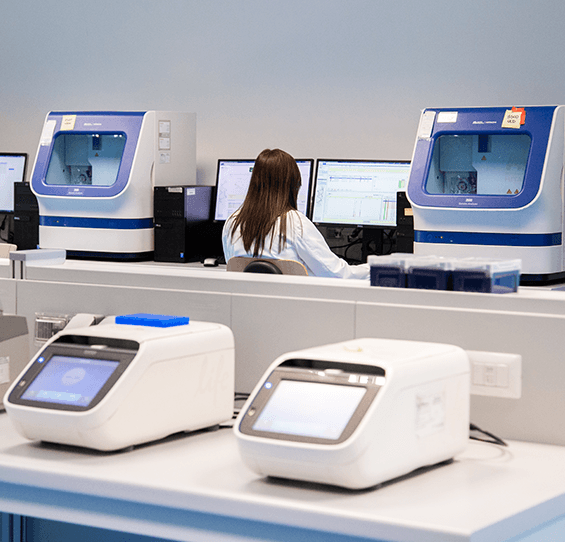 A scientist working at a computer in a genetics laboratory, with DNA analysis machines on the benches